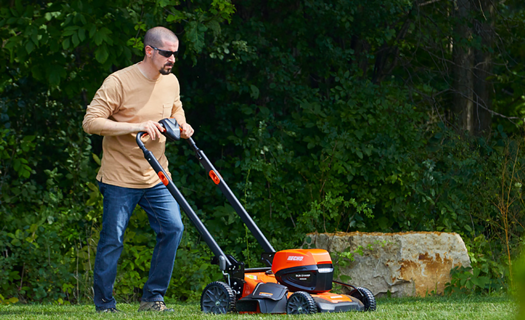 A man uses a self-propelled lawn mower to cut grass.