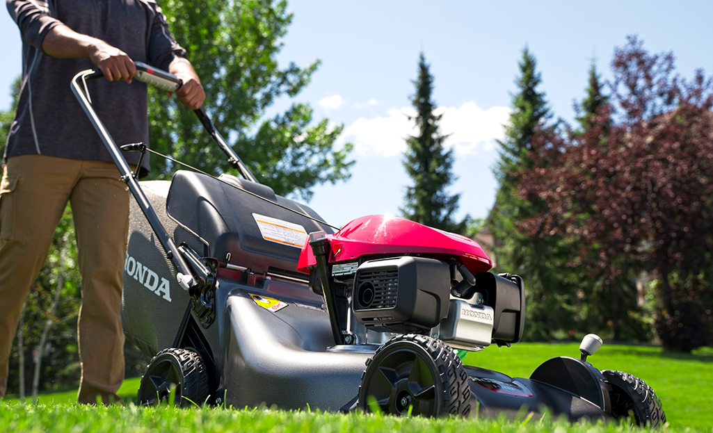 A person cuts a large lawn with a gas-powered, self-propelled mower.