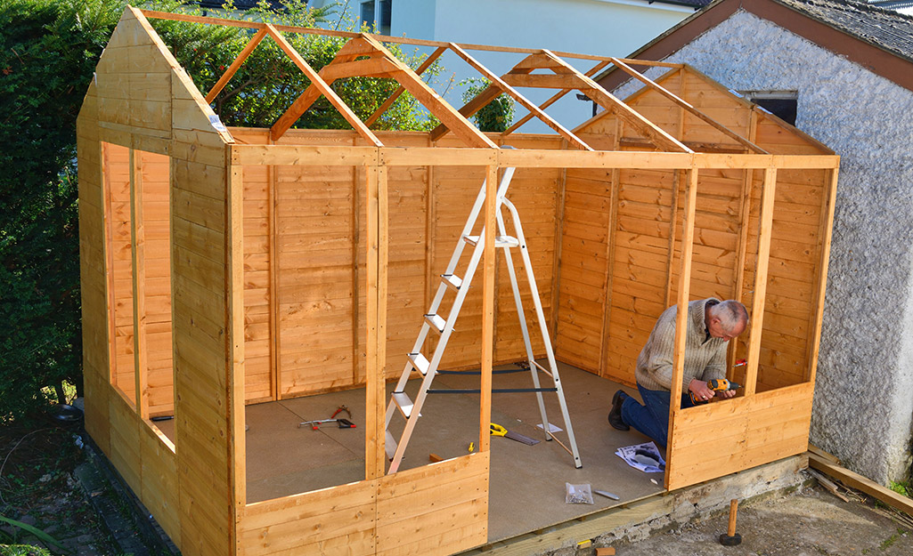 A man building the walls of a wood shed. A man building the walls of a wood shed.