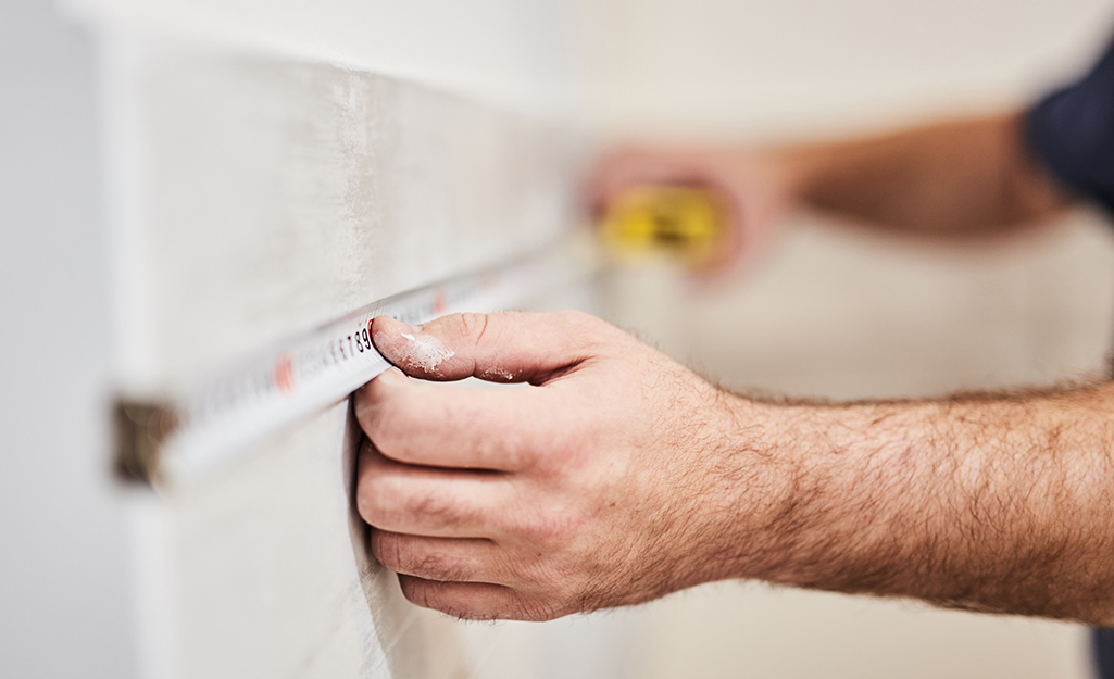 A person measuring a shower wall.
