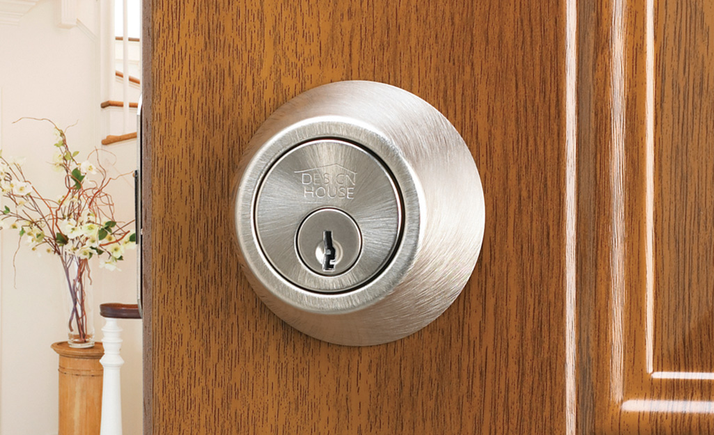 A deadbolt lock can be seen on the wooden door of a house.