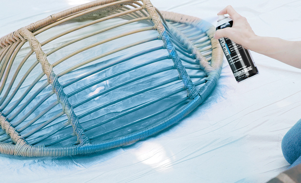 A person outside sprays paint onto a wicker chair.