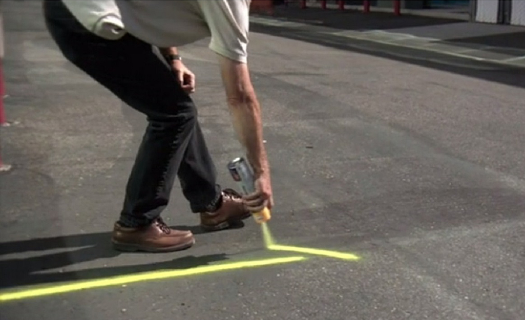 A person uses bright yellow spray paint to mark the pavement with lines.