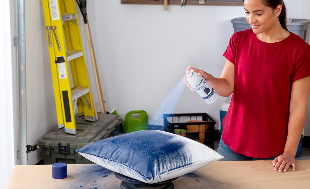A woman sprays a fabric pillow with fabric spray paint.