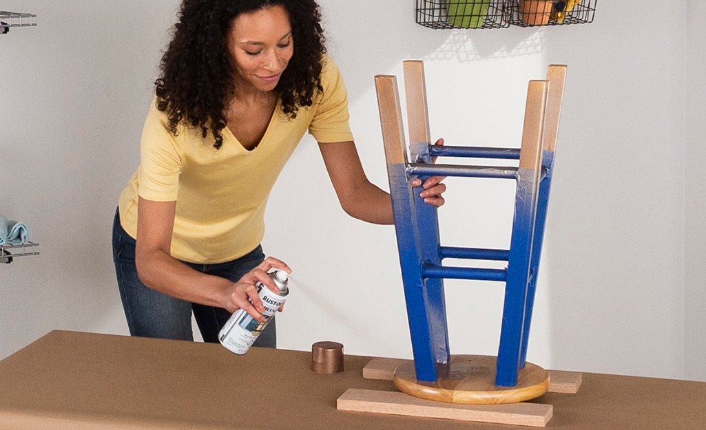 A woman paints a stool with spray paint.
