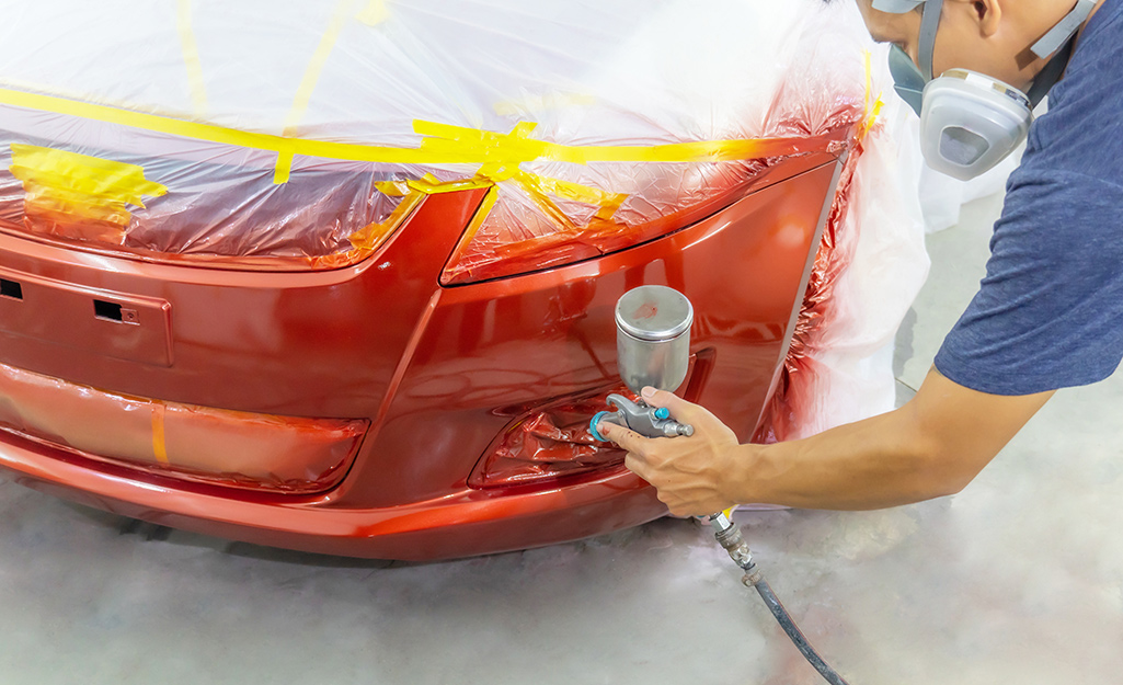 A person sprays a car with red paint.