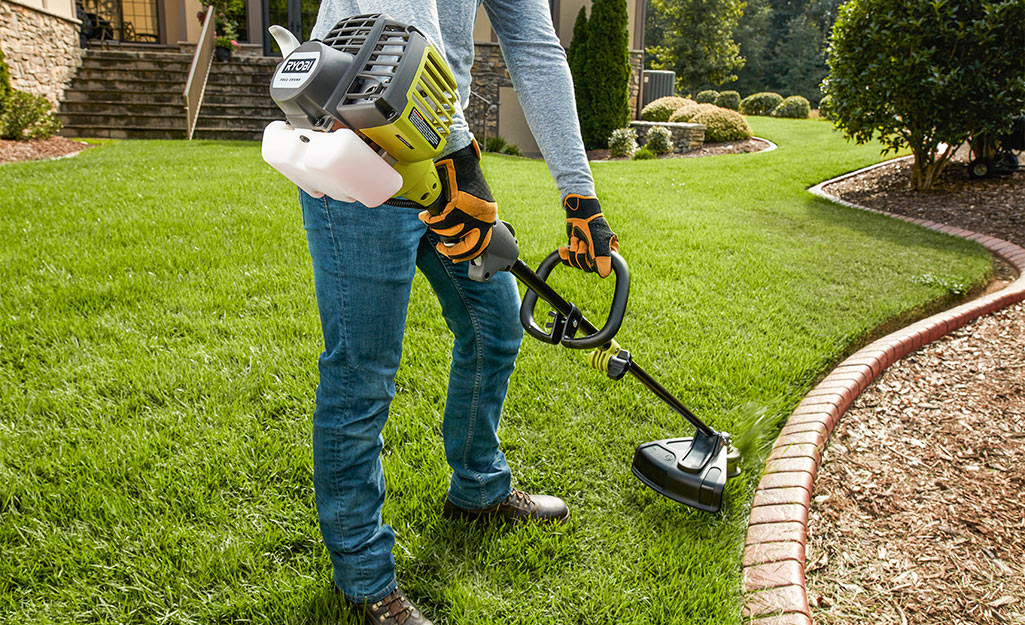 A person uses a gas string trimmer to edge flower beds.