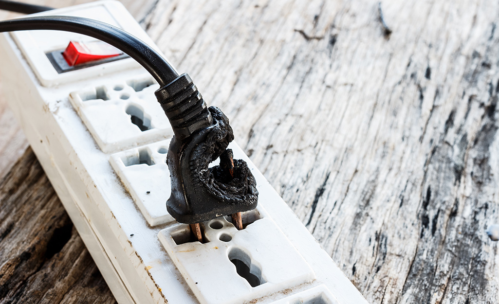 A worn, frayed plug plugged into a power strip.