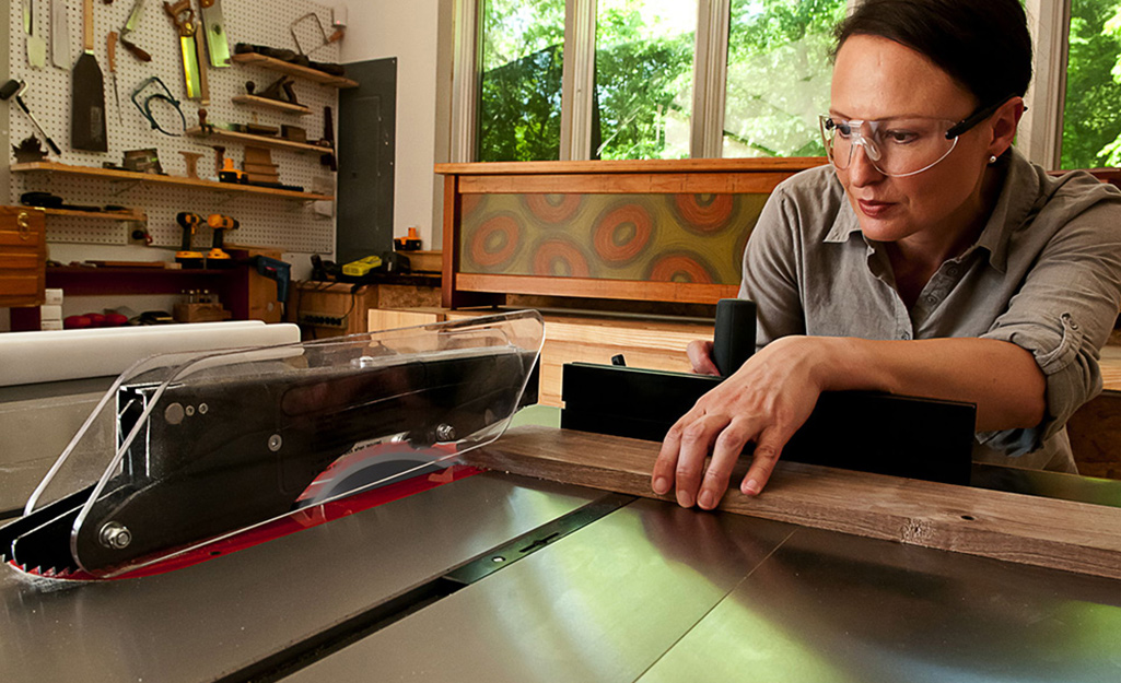 A person cuts a piece of wood trim with a table saw.