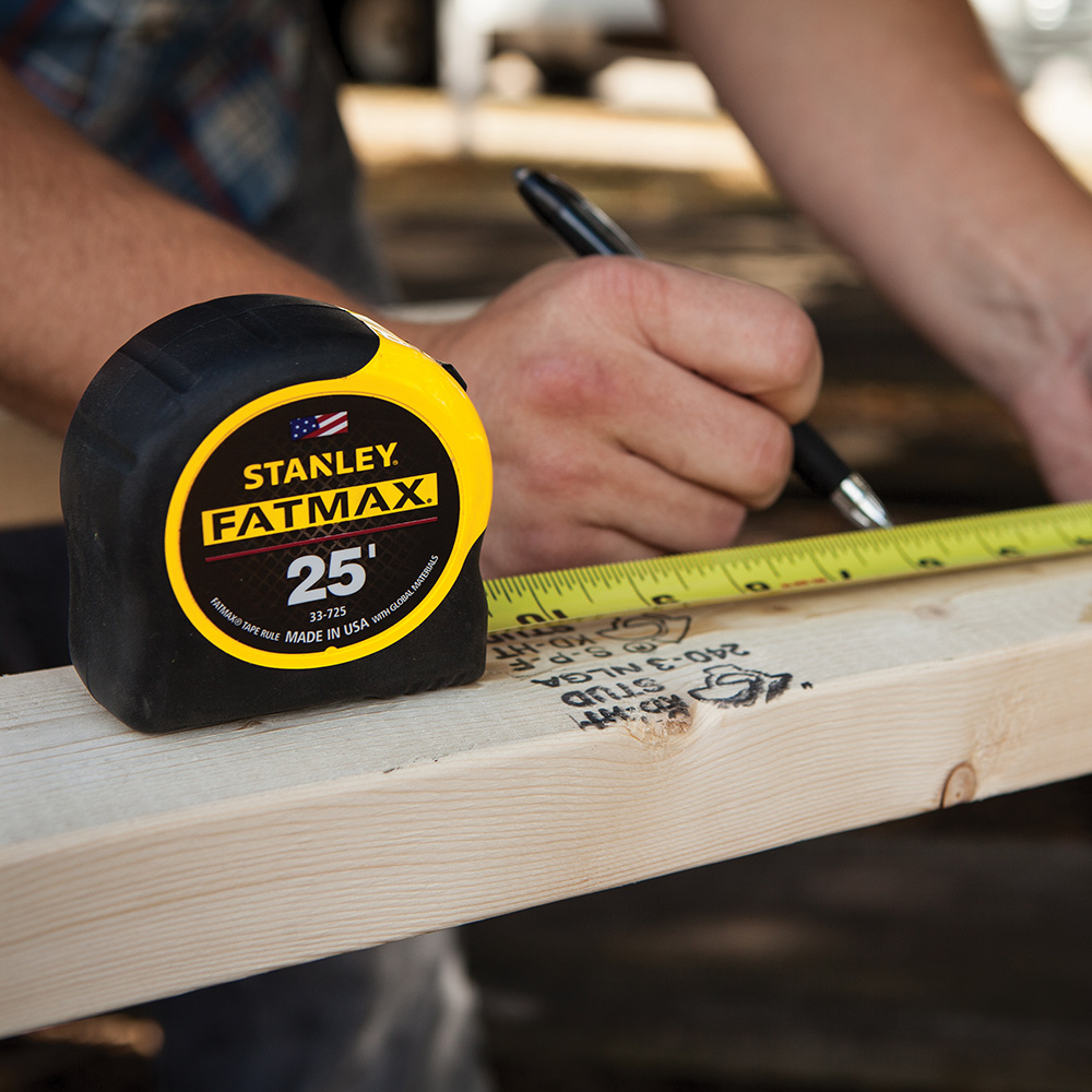 A person measuring a piece of lumber with a tape measure.