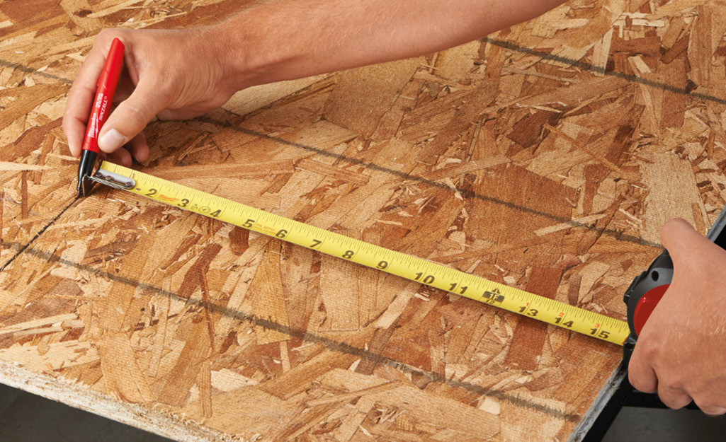 A person using a tape measure to mark lumber.