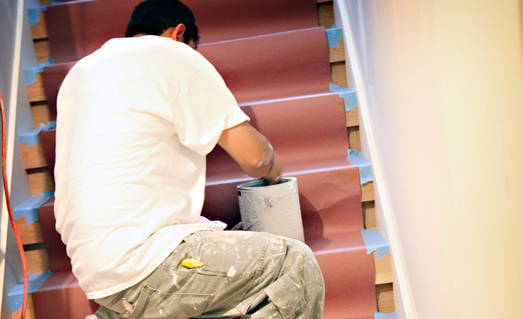 A man putting drop cloth on stairs.