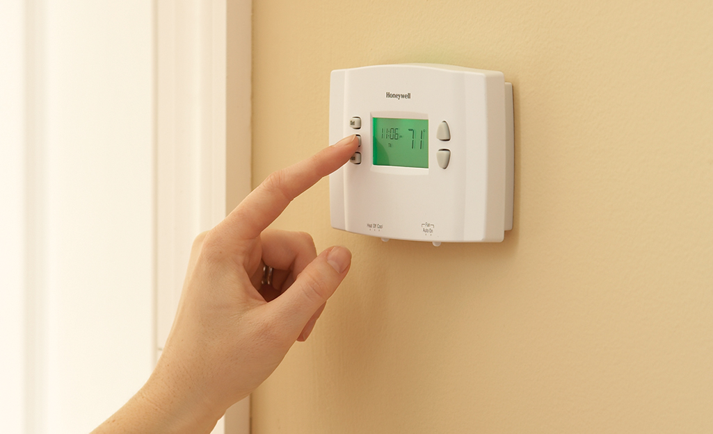 A person pressing a button on a manual thermostat.