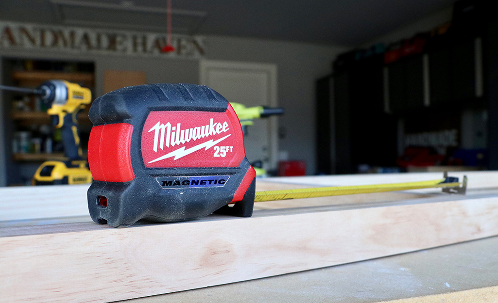 A tape measure sits on a piece of lumber in a garage. A tape measure sits on a piece of lumber in a garage.