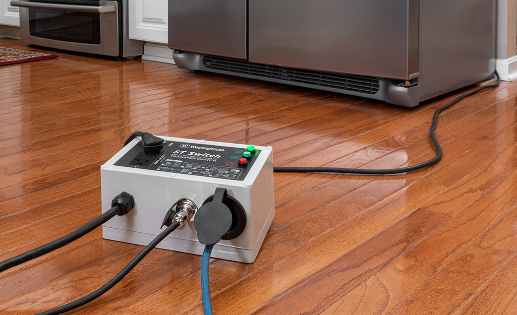 A transfer switch sits on the wood floor of a kitchen.