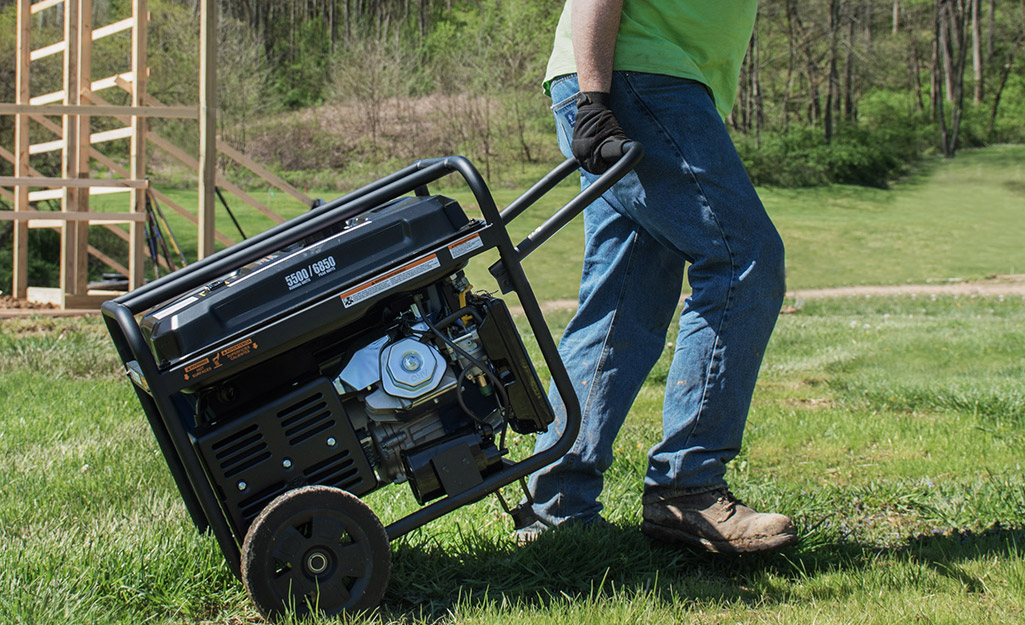 A man pulls a portable generator along grass-covered ground. 