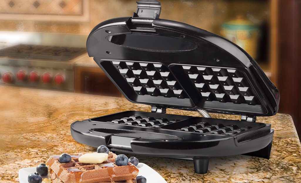 A classic waffle maker with a cooked waffle in it, sitting next to a cooked waffle topped with fruit