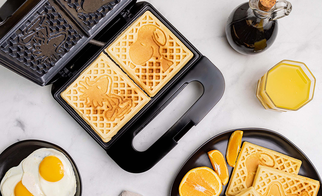 A double waffle maker with a cooked waffle inside sitting next to a plated waffle and eggs