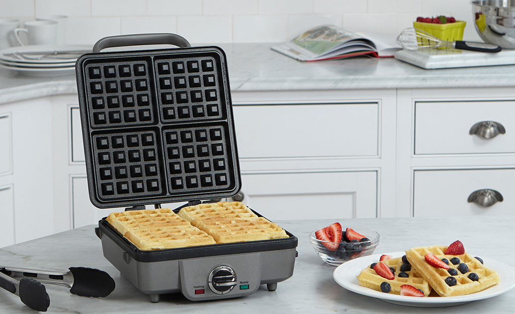 4-slice waffle maker with a cooked waffle inside and one plated off to the side