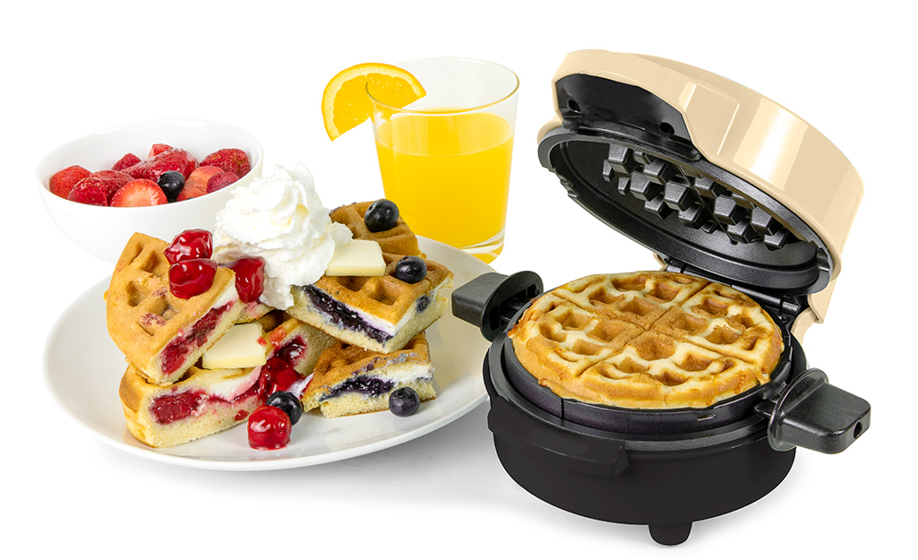 A mini waffle maker with waffles covered in fruits and cream.