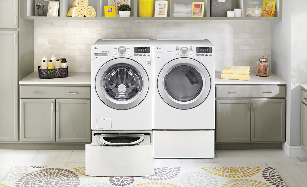 A washer and dryer on laundry pedestals with one pedestal drawer open.