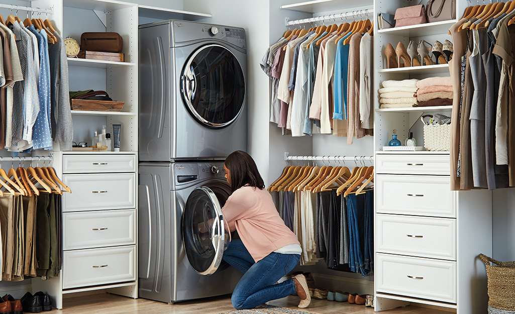 A woman kneels on the floor to unload a stacked washing machine.