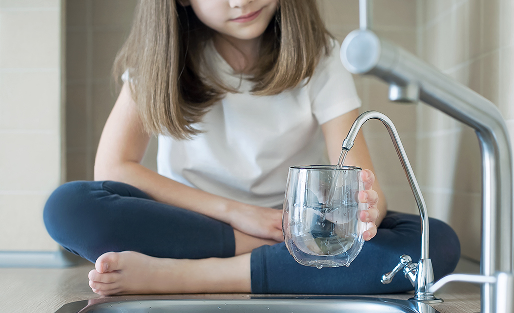 A child using a water dispenser out of a kitchen sink to pour a glass of water.