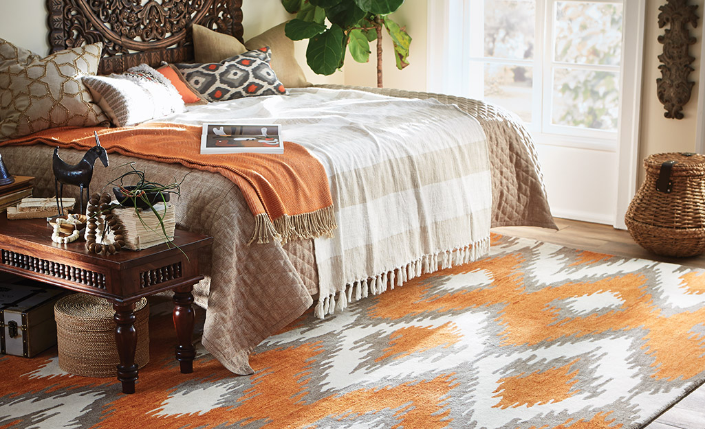 An orange, gray and white boho-style accent rug and a bed with layered bedding in similar colors. 