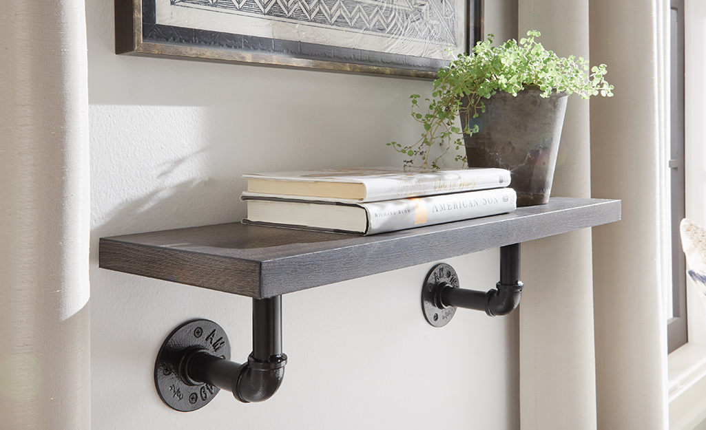 A bookshelf made of wood and metal piping hangs from a wall.