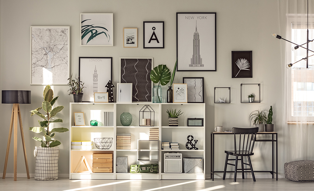 A bookcase filled with books and personal items sits under a gallery wall. 