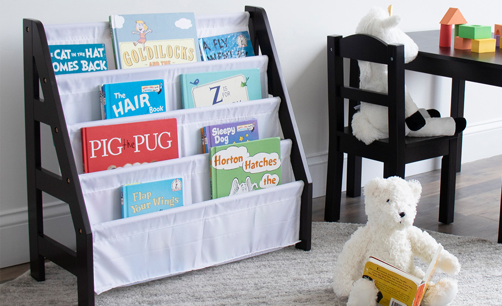 A black bookcase is decorated with white curtains in a child's play room.