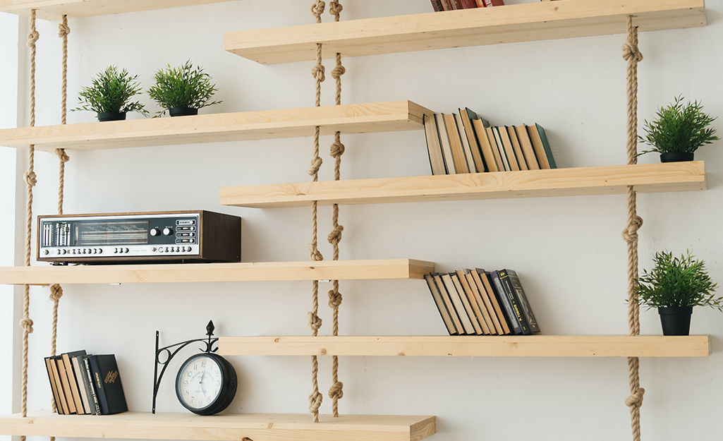 A bookself made of plywood and rope hangs from a wall. 