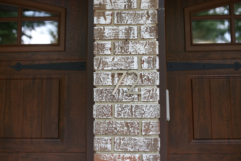 Address house numbers on a brick column between two wooden garage doors.