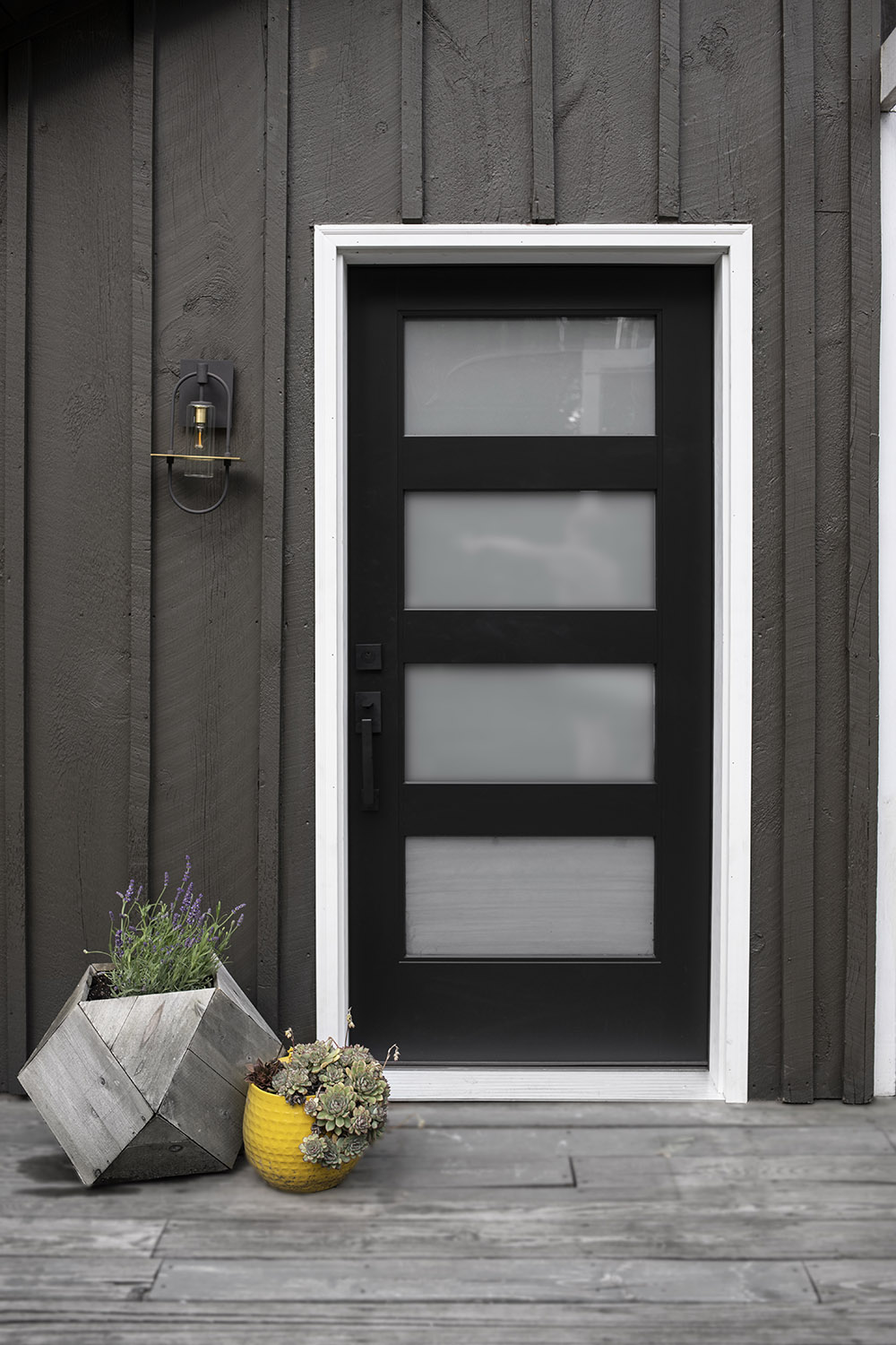 A pair of planters sit outside a black and glass modern front door.