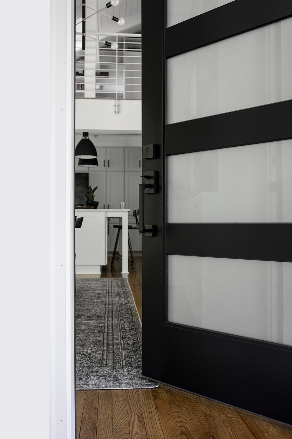 A black and glass front door with black hardware opens to a room with hardwoods.