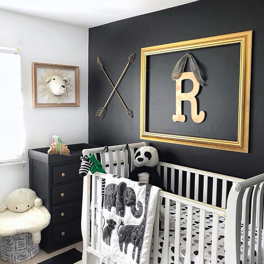 A boy's nursery with an accent wall painted in a dark color and his initial framed and hung over the crib. 