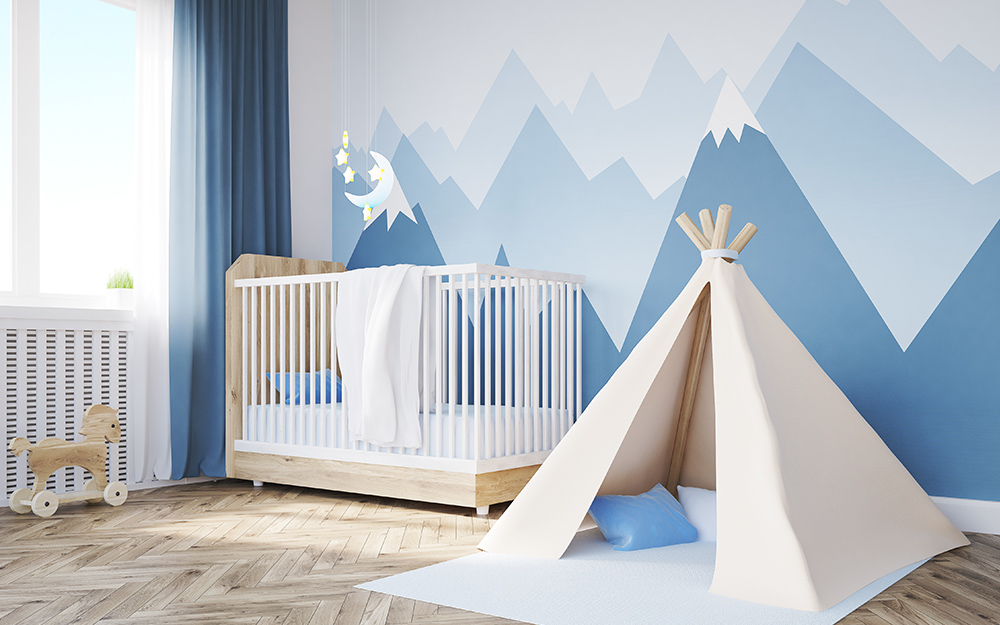 A boy nursery decorated in blue and white with a small tent for play and a wall mural of mountains.