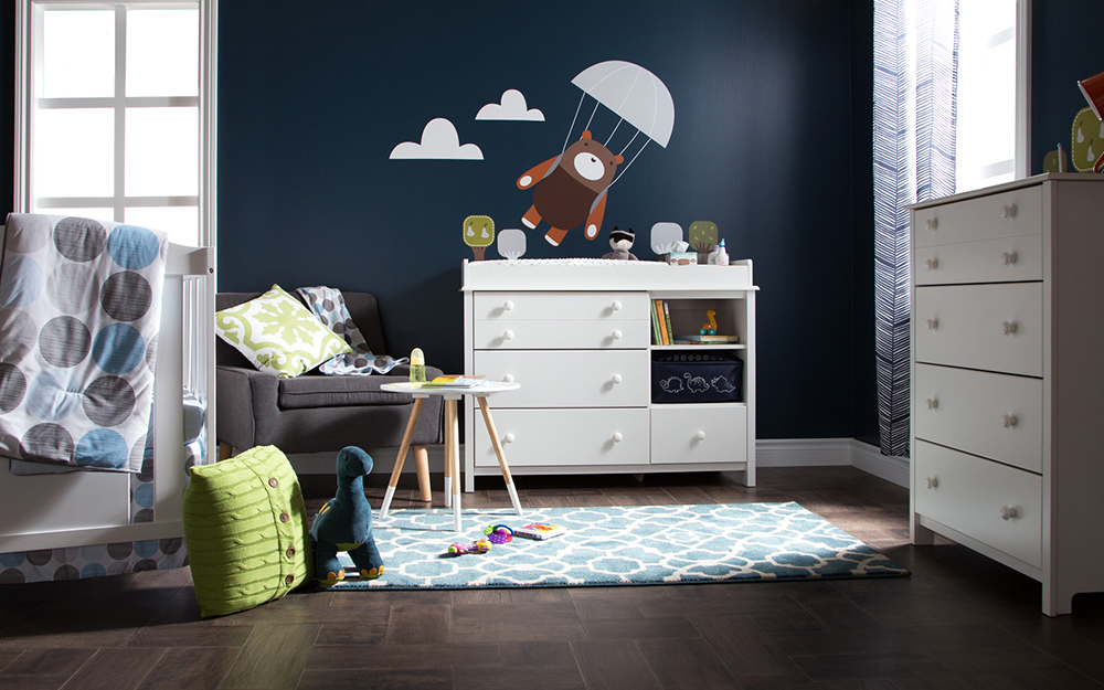 A boy's nursery with dark walls, white furniture and a decal of a bear in a parachute.