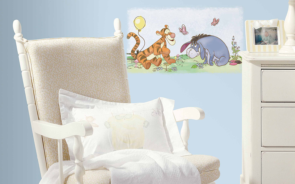 A boy nursery with blue walls, a white rocking chair and Winnie the Pooh characters on the wall.