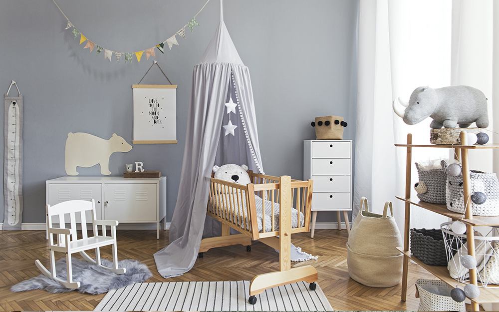 A boy's nursery with gray walls, white furniture and gray, a gray crib canopy and a gray and white area rug.