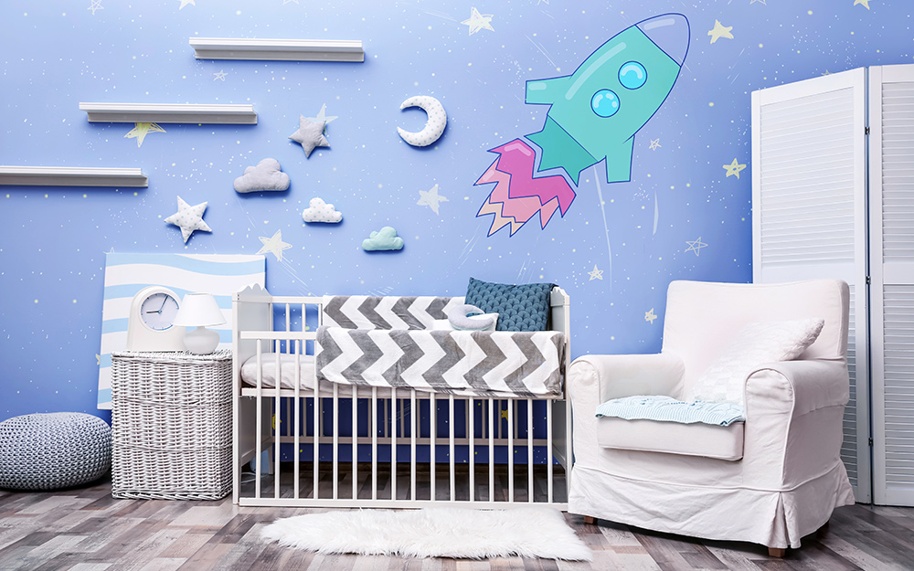 A boy's nursery with blue  walls, a white chair, gray and white accessories and a rocket ship on one wall.