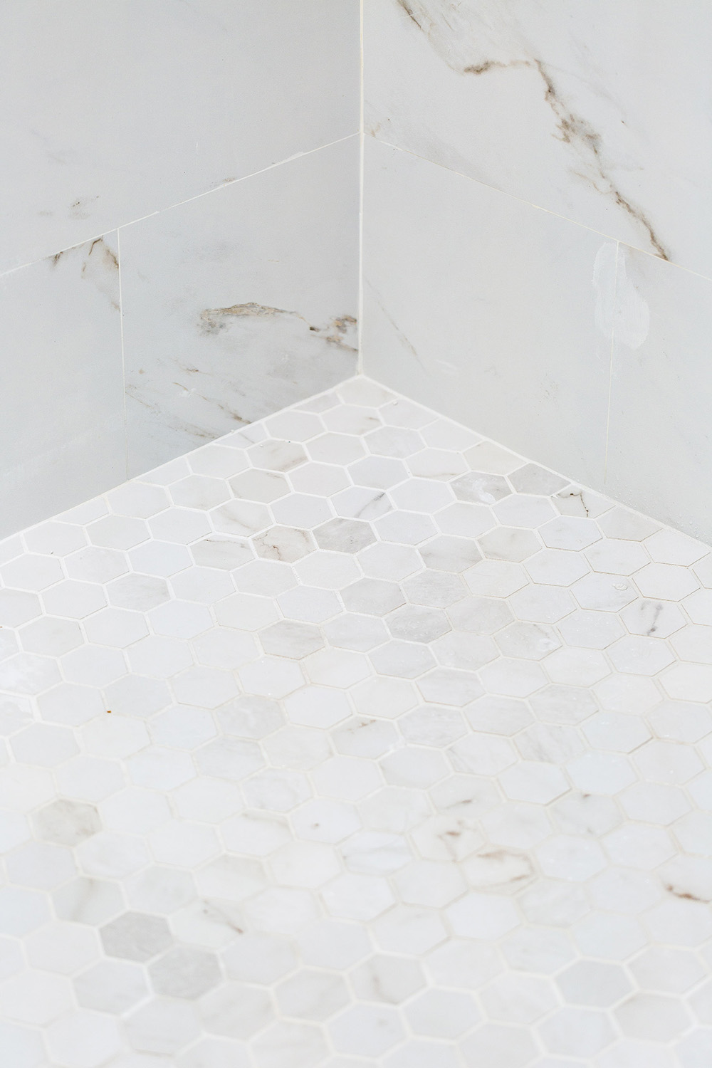 A shower floor with white hexagon tiles.