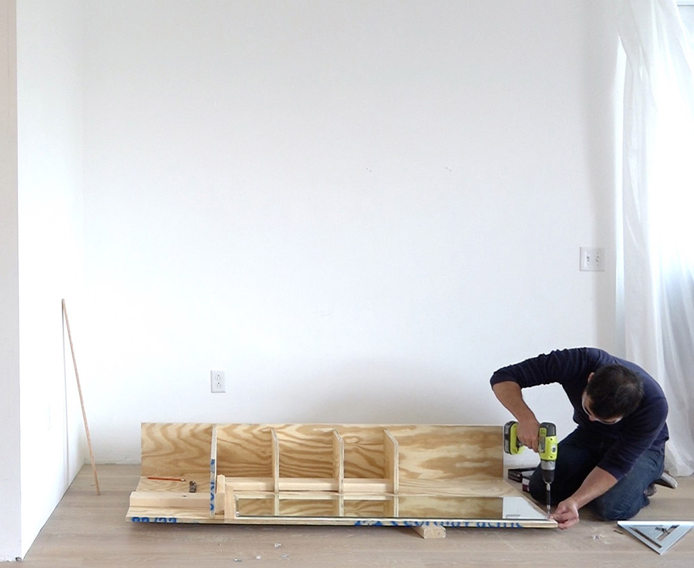 A person connecting a mirror onto plywood 