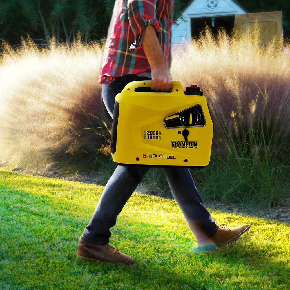Someone carrying a yellow inverter generator across a lawn.