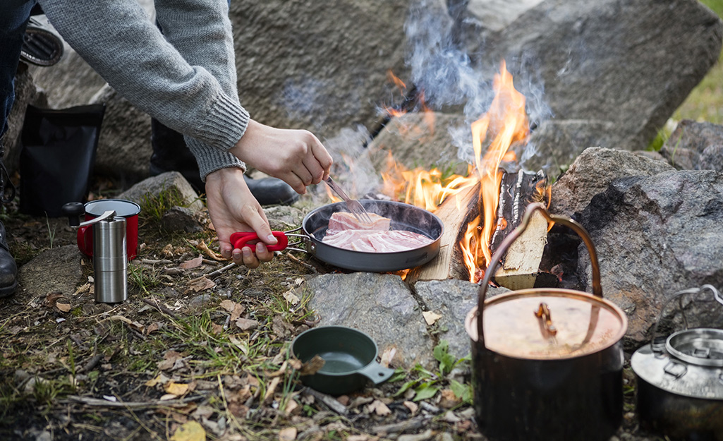 A camper cooks a meal in a pan over an open campfire.