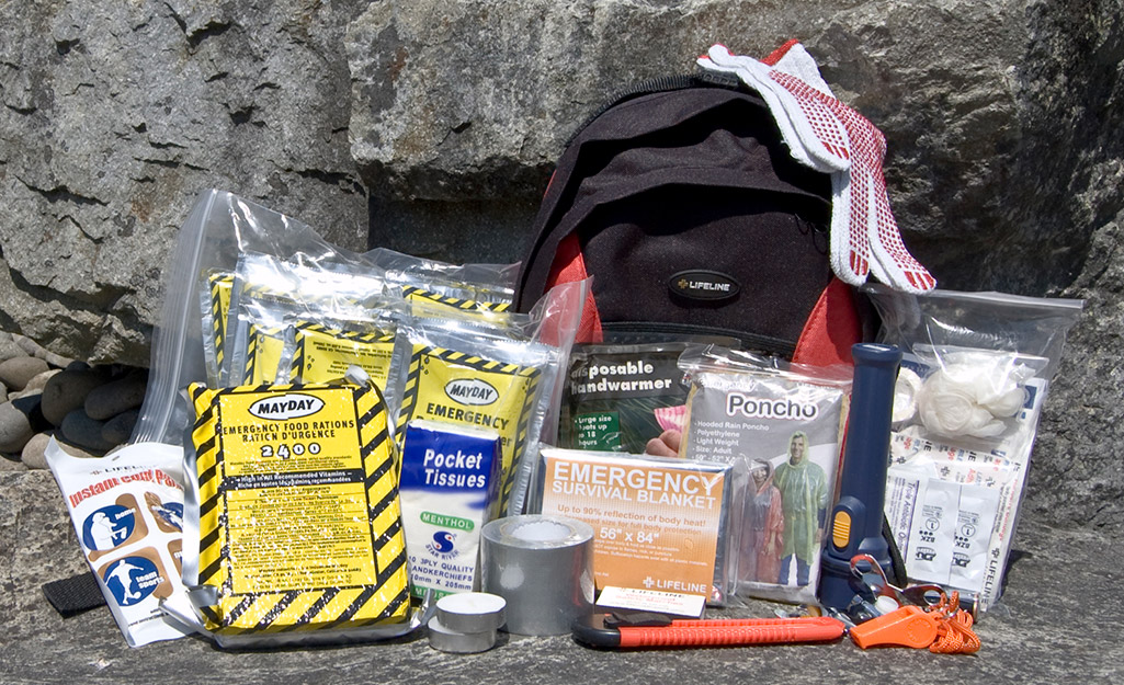 A collection of first aid and emergency items on the ground next to a backpack.