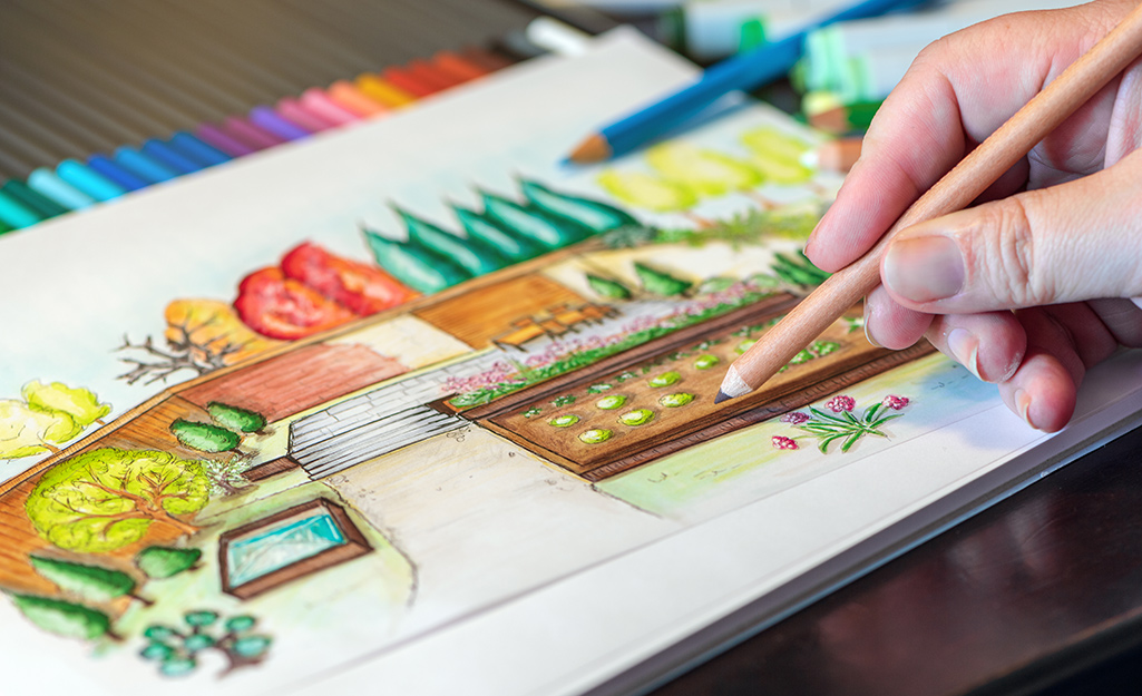 Someone using colored pencils to design an outdoor garden plan.