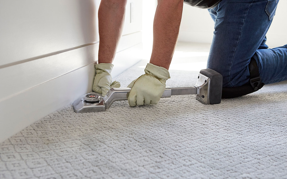A person securing new carpet to the floor