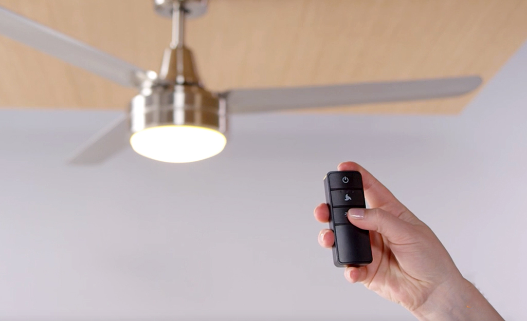 A person uses a remote control on a ceiling fan.