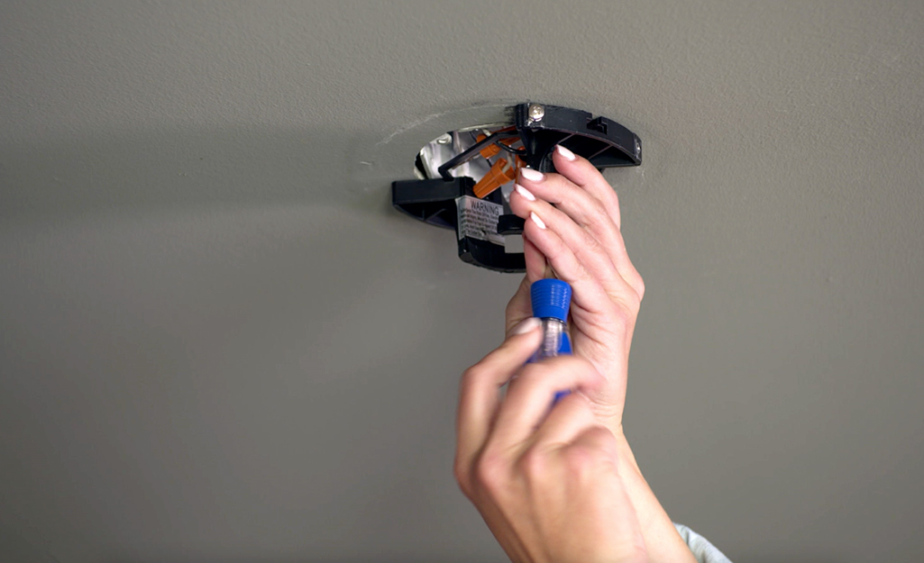A person disconnects electricity to a ceiling fan switch.